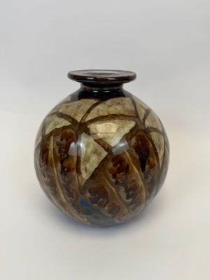un vase brun et noir posé sur une surface blanche