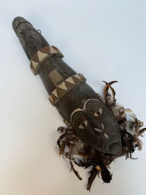 un objet en bois orné de plumes, posé sur une surface blanche