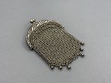 un porte-monnaie en métal argenté, entouré d'une chaîne, posé sur une surface grise