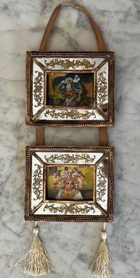 two picture frames hanging on the wall with tassels