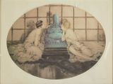 two women sitting on the floor next to a blue vase
