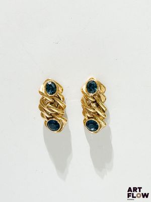 une paire de boucles d'oreilles en or ornées de pierres bleues, posées sur un fond blanc