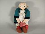 une petite poupée assise par terre avec une pelote de laine
