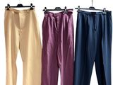 trois paires de pantalons suspendues à un portant, sur fond blanc