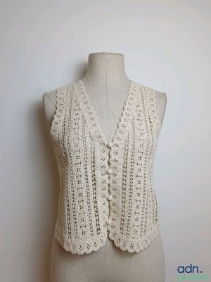 Le gilet est tricoté avec du fil blanc et présente un motif au crochet sur le devant.