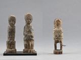three carved figurines of a man and a woman on a stand