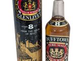 une bouteille de whisky posée à côté d'un carton sur une surface blanche