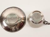 a silver cup and saucer sitting on a white table