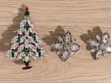 three christmas tree brooches on a wooden surface with a christmas tree in the background