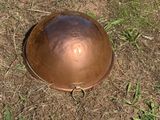 a large copper helmet on the ground in the grass