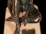 a bronze statue of a woman sitting on a wooden block