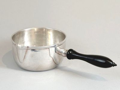 une casserole en argent avec une poignée noire posée sur une table blanche