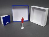 a small red figure standing in front of a white box