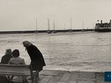 black and white photo of people sitting on a bench by the water