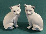 deux chats en céramique blanche assis l'un à côté de l'autre sur une surface verte