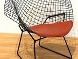 a black wire chair with a red seat on a wooden floor