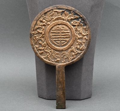 un ancien miroir chinois en bronze posé sur un socle, sur une surface grise