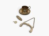 an assortment of silver objects including a tea cup, saucer, and spoon