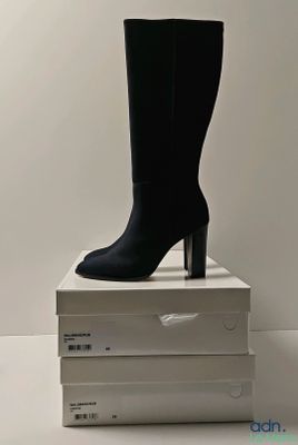 des bottes noires à talons hauts posées sur une pile de cartons blancs