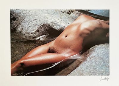 a nude woman laying on a rock in the water