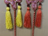 trois bâtons décoratifs ornés de pompons et de perles, posés sur une table