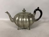 une théière ancienne en argent avec une poignée noire sur une surface blanche