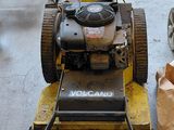 a lawn mower sitting on the sidewalk next to a car