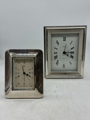 une petite horloge en argent posée à côté d'une autre horloge en argent, plus petite