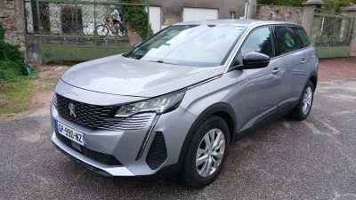 La voiture argentée est garée sur le parking devant la maison.