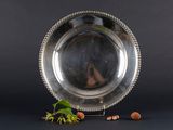 an antique silver plate with beading and nuts on a black background