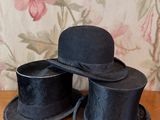 deux chapeaux haut-de-forme noirs posés sur une table en bois devant un papier peint à motifs floraux