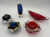 four different colored glass objects are arranged on a white surface