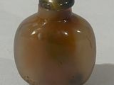 une petite bouteille en verre avec un bouchon doré, posée sur une surface blanche
