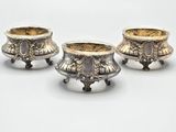 trois vases en argent empilés les uns sur les autres sur une surface blanche