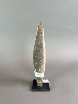 sculpture représentant une pointe de flèche en pierre posée sur un socle noir, sur fond gris