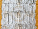 a close up of a yellow and white scarf on a bed