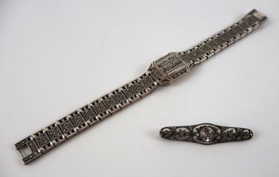 une image représentant une montre en argent et un bracelet en argent posés sur une surface blanche
