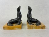 une paire de serre-livres en bronze représentant des otaries, posés sur des socles en marbre
