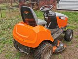 an orange riding lawn mower sitting in the grass next to a barn