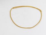 un collier à chaîne en or posé sur une surface blanche
