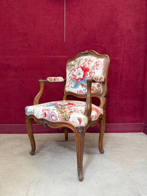 une chaise dont l'assise est recouverte d'un tissu à motifs floraux, placée devant un mur rouge