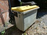 une poubelle avec un couvercle jaune posée dans l'herbe