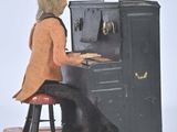 a doll sitting at a piano with a teddy bear on it