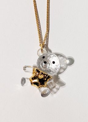 un petit ours en peluche avec une chaîne en or, posé sur une surface blanche