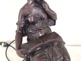 statue of a woman reading a book on a table with a lamp