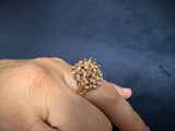 an image of a woman ' s hand holding a gold ring with pink and green stones