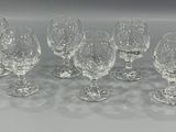 six crystal wine glasses lined up in a row on a white surface