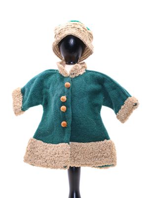 une poupée vêtue d'un manteau vert et d'un chapeau, posée sur un mannequin noir