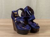 purple wedged sandals with gold buttons on a wooden surface