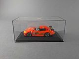 an orange car in a clear display case on a gray surface